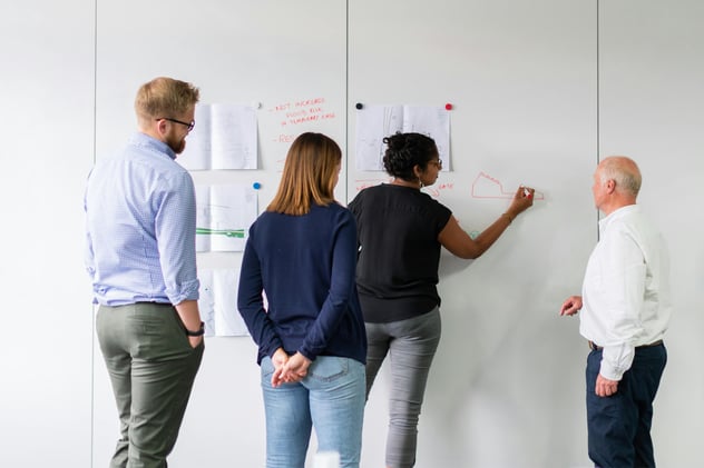 Four team members at an operational excellence workshop write on a whiteboard